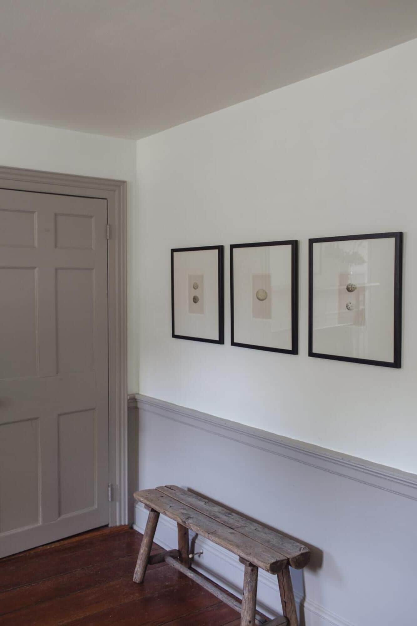 Un couloir avec une porte blanche, un banc en bois et trois tableaux encadrés accrochés au mur.