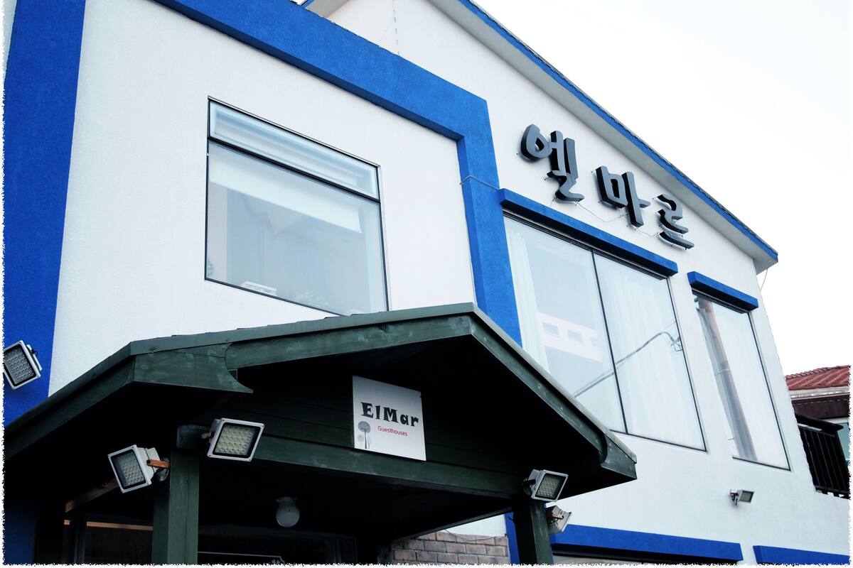 A building with a blue and white facade, featuring large windows and a sign that reads "EIMar Guesthouses".