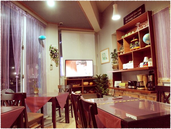 Una sala de estar acogedora con un televisor de pantalla plana, comedor con sillas y una mesa, y una estantería con diversos objetos.