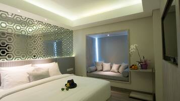 A modern bedroom with a large bed, a window seat with cushions, a decorative wall panel, and a mounted TV.