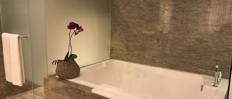 A modern bathroom with a glass-enclosed shower, a white bathtub, and a woven basket holding a purple orchid.