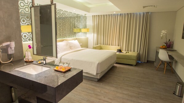 A hotel room with a large bed, a separate sofa, a desk, and a bathroom with a sink and mirror. - Daun Bali Seminyak Hotel (Keroboken Kelod)