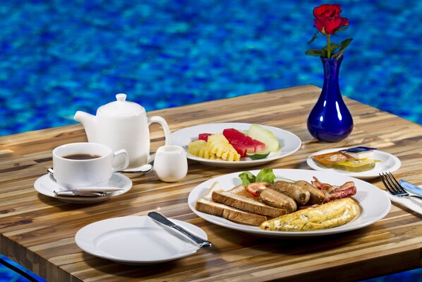 A breakfast table with plates of toast, eggs, bacon, and fruit, a teapot, cups, and a vase with a rose. - Daun Bali Seminyak Hotel (Keroboken Kelod)