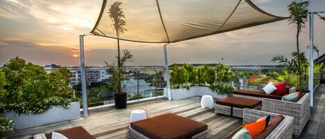 A rooftop terrace with wicker furniture, a large canopy, and a view of the cityscape.
