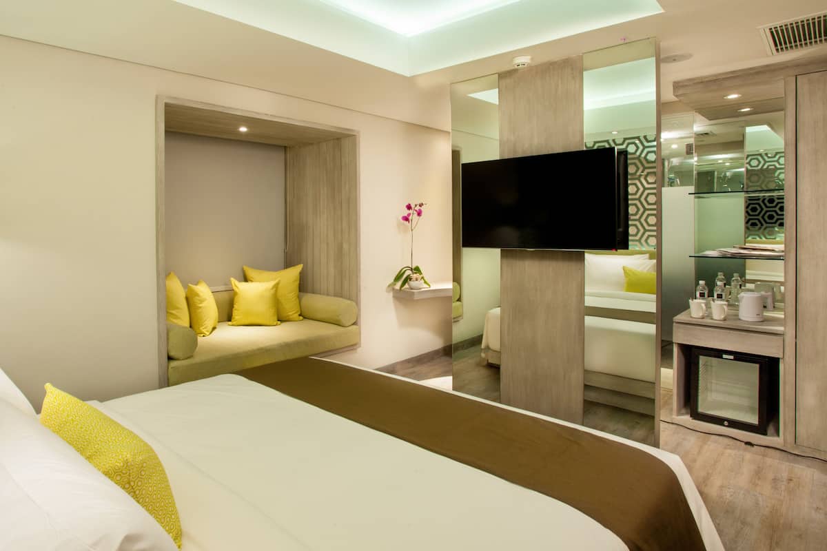 Una habitación de hotel con una cama grande, un sofá con cojines amarillos, un televisor y un minibar.