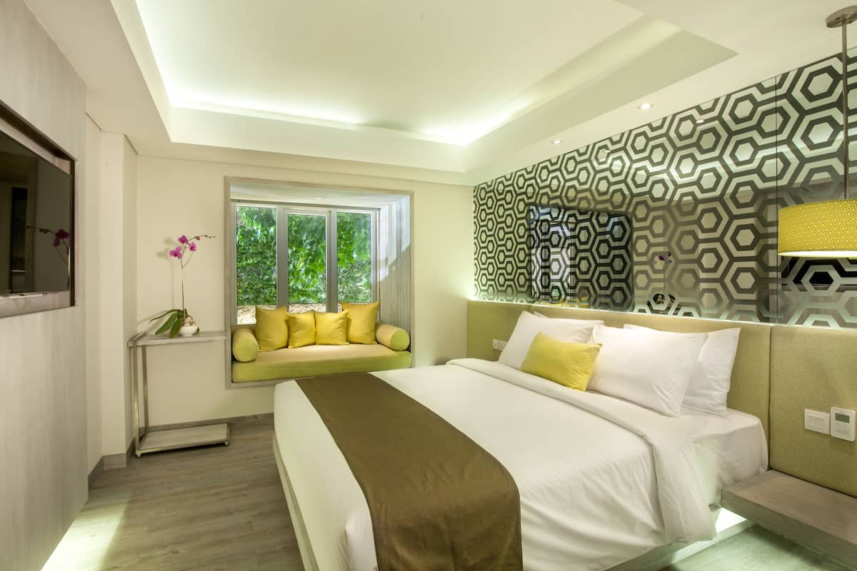Una habitación de hotel moderna con una cama grande, un asiento junto a la ventana y un papel tapiz estampado.