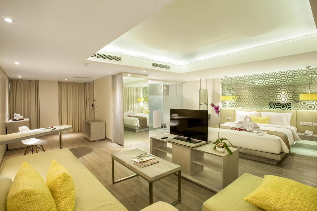 Una habitación de hotel moderna con sofá, mesa de centro, televisor y cama con cabecera estampada.
