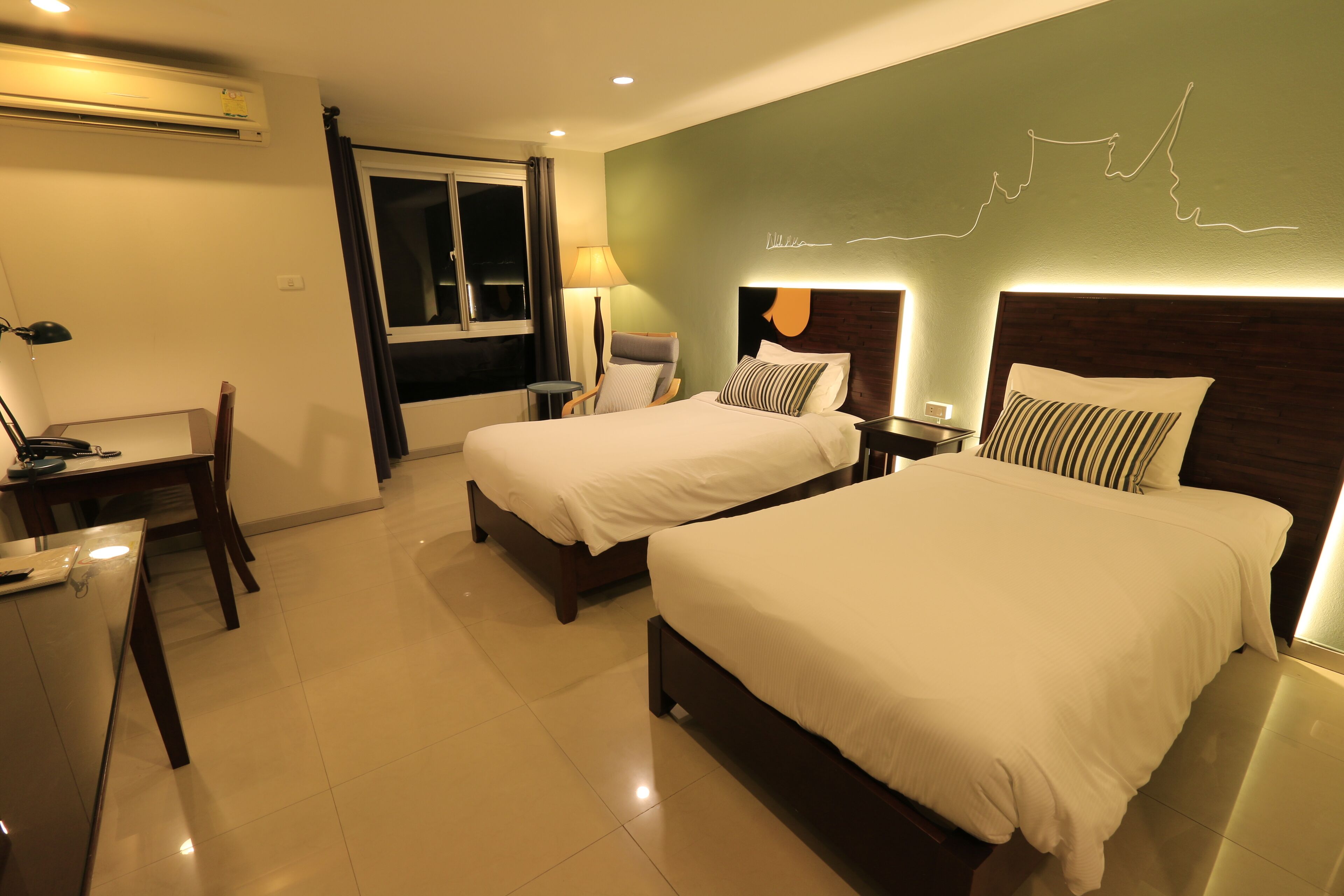A hotel room with two beds, a desk, a chair, and a window with curtains.