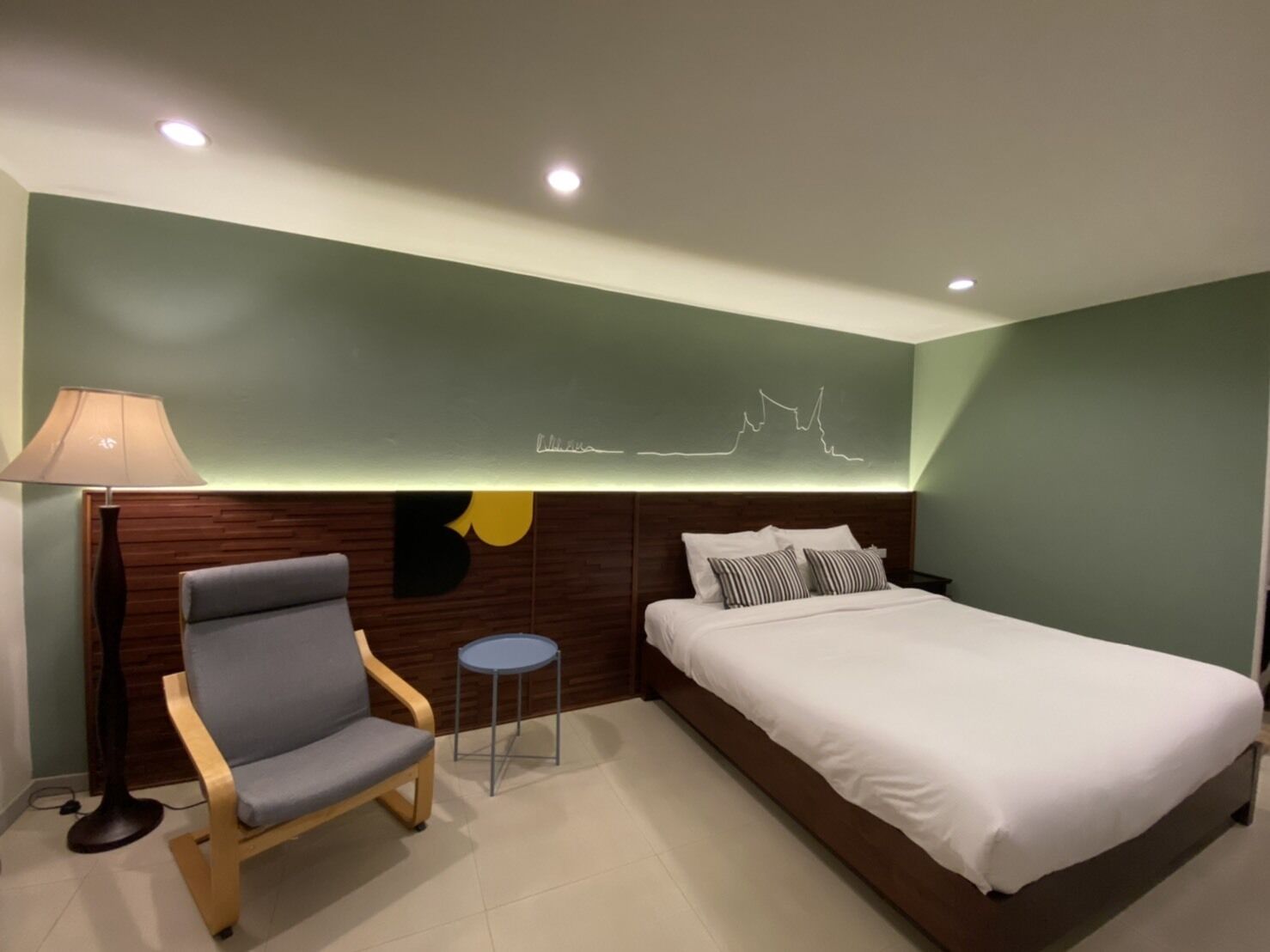 A modern bedroom with a bed, a chair, a small table, and a wall-mounted light fixture.