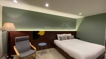 Un dormitorio moderno con cama, una silla, una mesita y un aplique de pared.