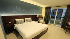 Hotelkamer met een groot bed, een houten hoofdbord, nachtkastje, stoel, lamp en uitzicht door een glazen deur.