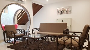 Una sala de estar moderna con un sofá, dos sillones, una mesa de centro de vidrio y un espejo decorativo.