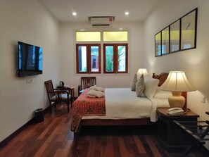 A hotel room with a bed, a desk, a chair, a TV, a lamp, and a window with a view of greenery. - Heeren Straits Hotel (Malacca City)