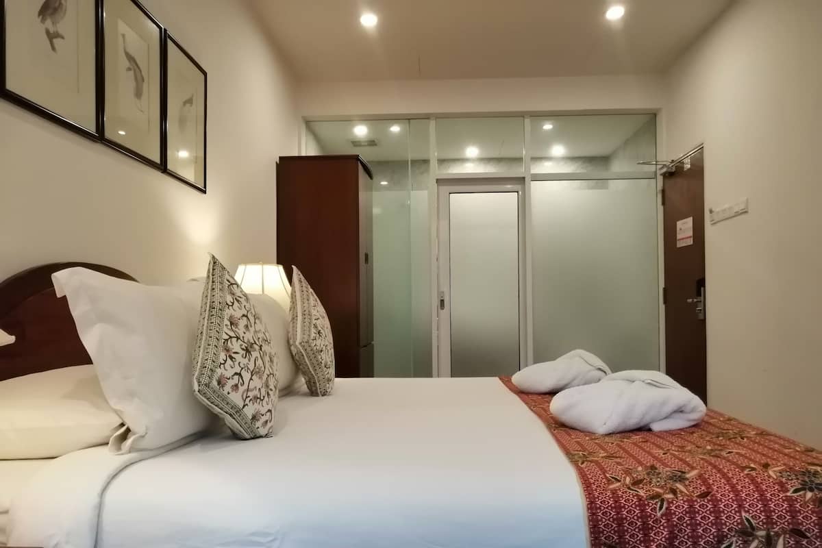 Une chambre d’hôtel comprenant un lit, des oreillers, une table de chevet, une lampe, une armoire et un miroir.