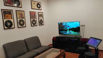 Uma sala de estar com sofá, mesa de centro, TV em um suporte e discos de vinil emoldurados na parede.