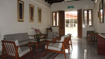 Un espace d’accueil comprenant un canapé, des fauteuils, une petite table ornée d’un vase de fleurs et un panneau indiquant l’entrée du hall.