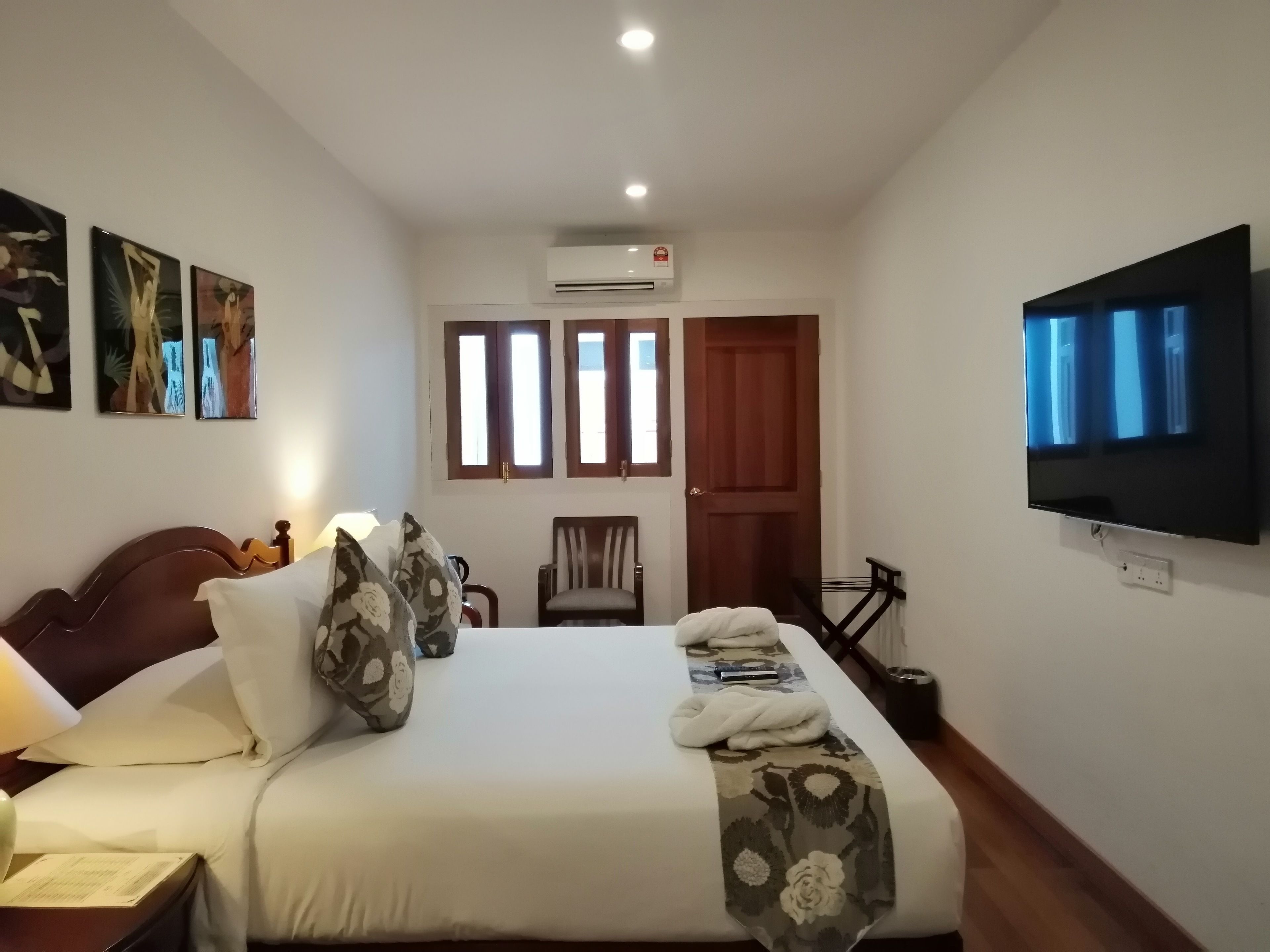 A hotel room with a bed, a TV, a chair, and artwork on the wall.