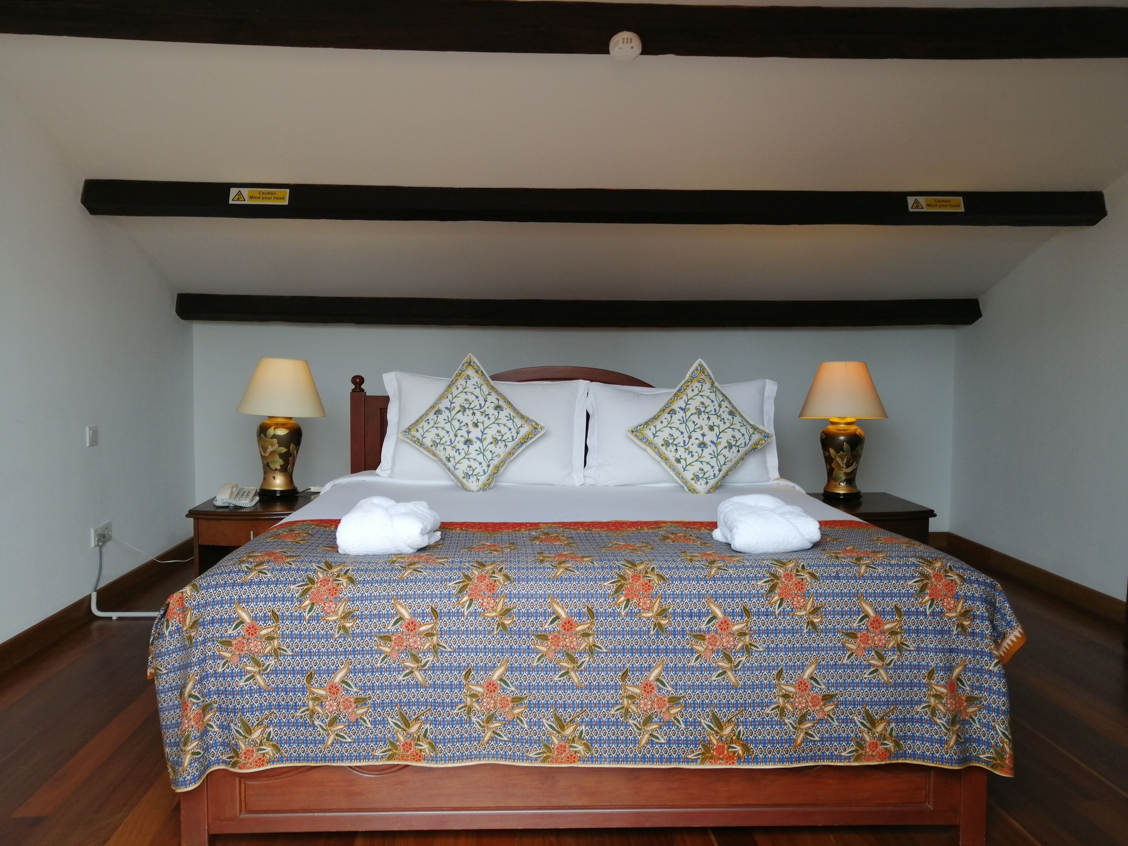 Uma cama bem arrumada com roupa de cama estampada com flores, duas luminárias de cabeceira e um telefone na mesinha de cabeceira.