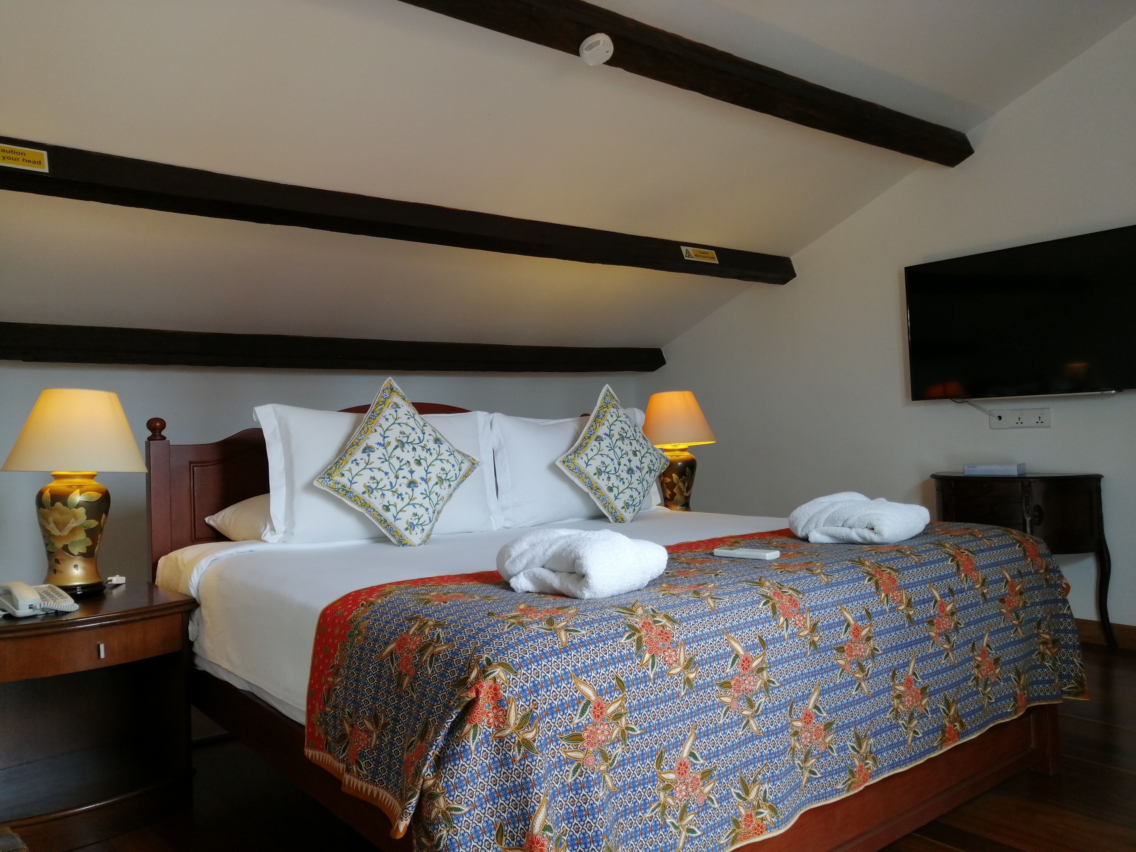 A hotel room with a large bed, two bedside lamps, a flat-screen TV, and a telephone on the nightstand.