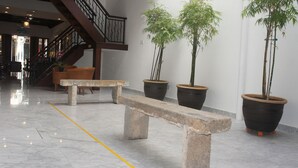 Un vestíbulo con suelo de mármol, un banco de piedra, plantas de bambú en macetas, muebles de mimbre y una escalera.