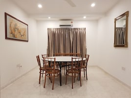 Un salón de conferencias con una mesa redonda, seis sillas, un equipo de aire acondicionado, un espejo grande y una obra de arte enmarcada en la pared.