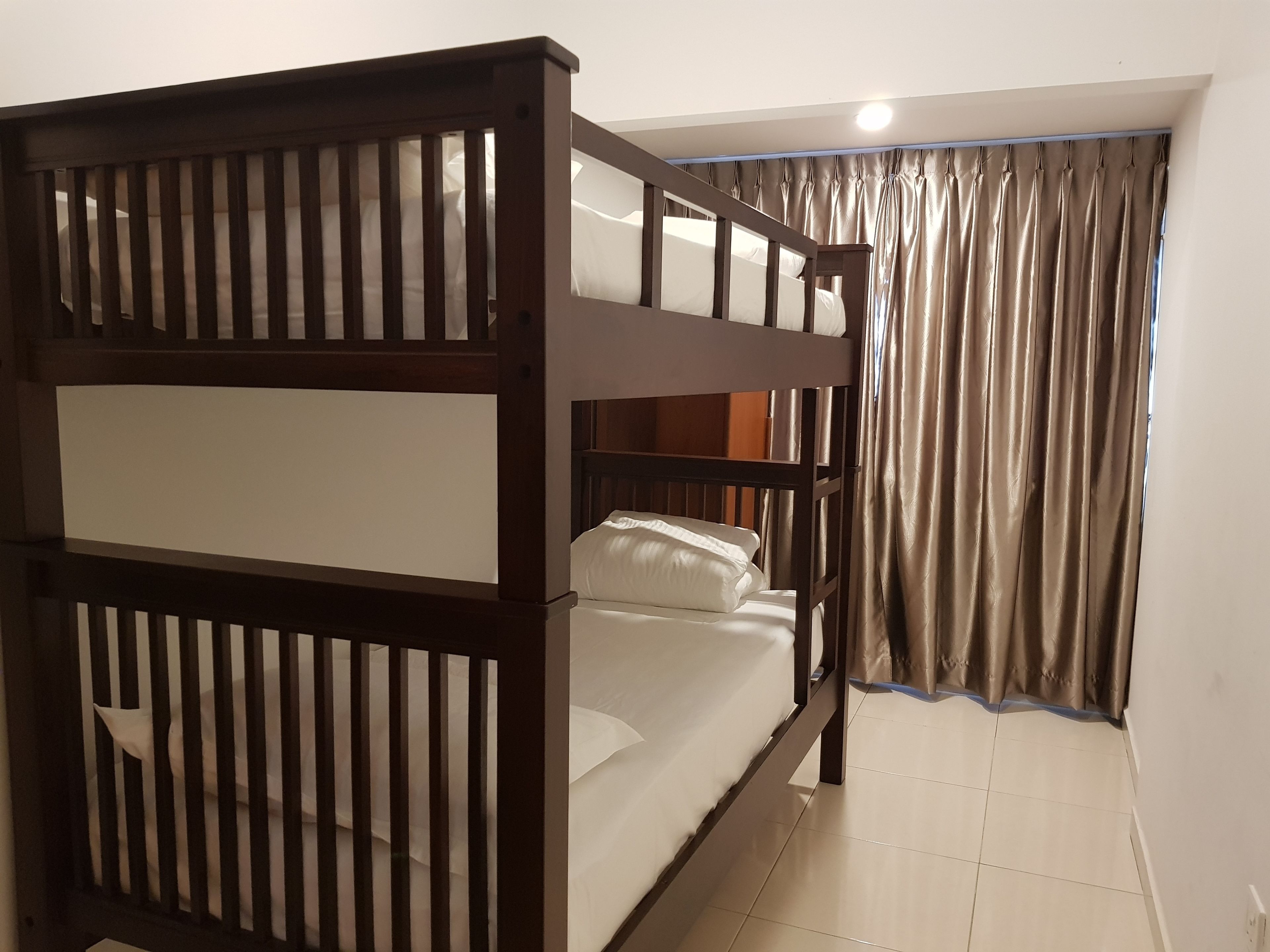 A bunk bed with a wooden frame and white bedding, a window with curtains, and a tiled floor.