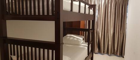 A bunk bed with a wooden frame and white bedding, a window with curtains, and a tiled floor.