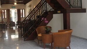 Un vestíbulo con escaleras de madera, mobiliario de mimbre y suelo de mármol.