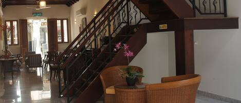 A lobby with a wooden staircase, wicker furniture, and a marble floor.