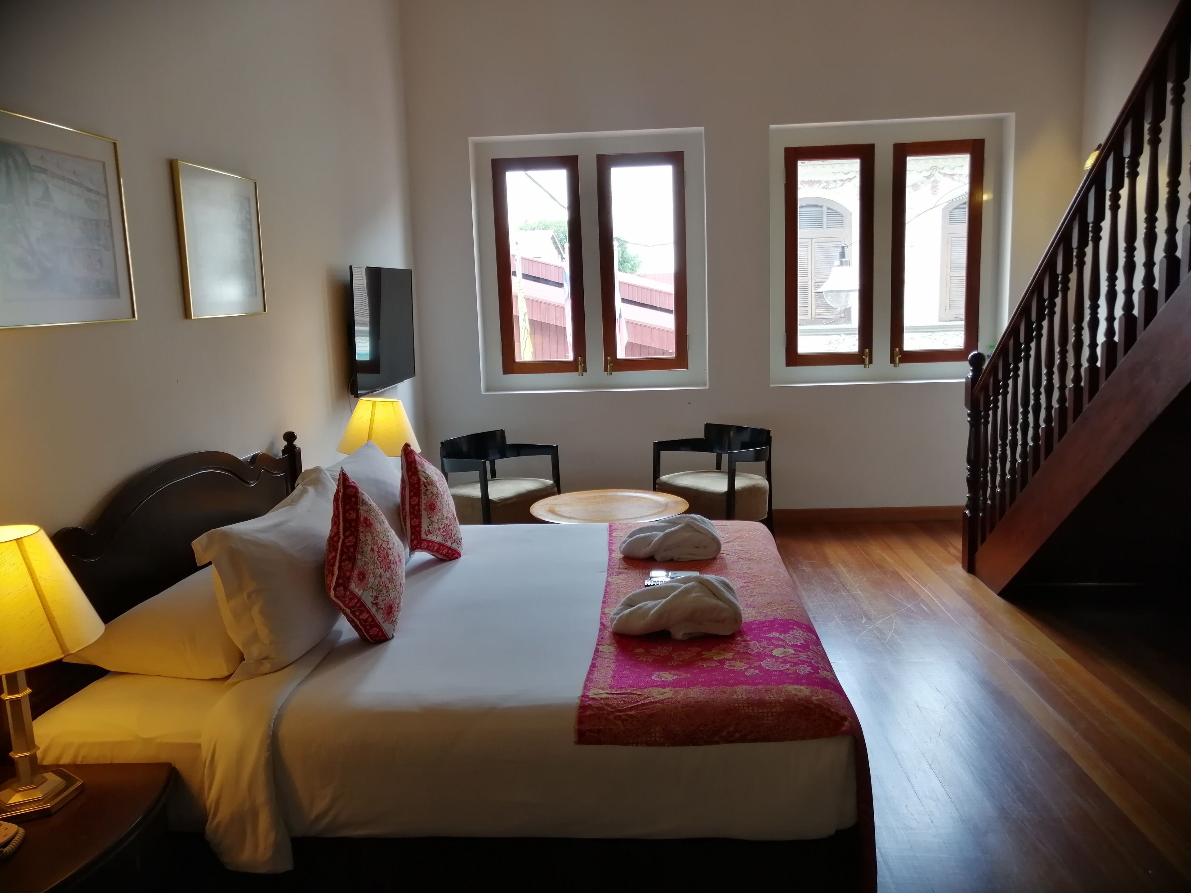 Habitación de hotel con cama, lámpara de noche, dos sillas, una mesita, televisor y una escalera.