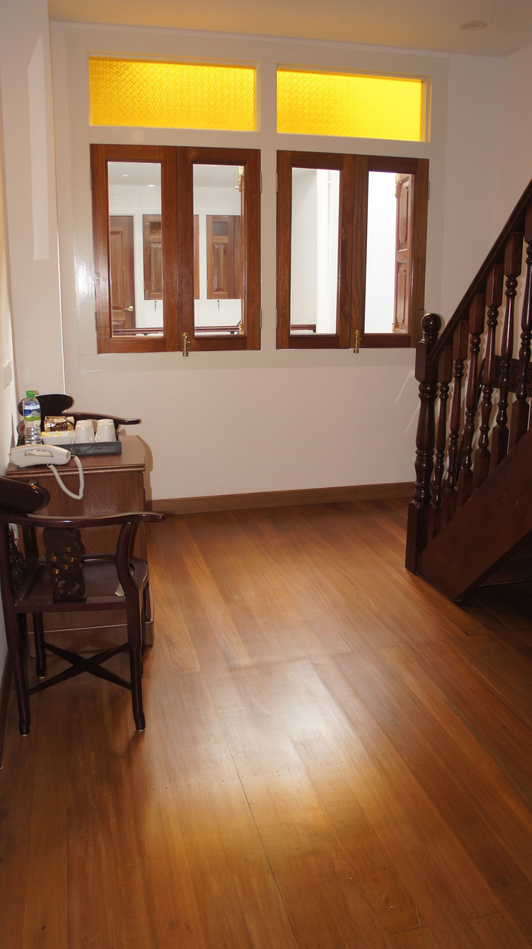 A room with wooden flooring, a staircase, and a window with wooden frames.
