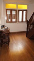 A room with wooden flooring, a staircase, and a window with wooden frames.