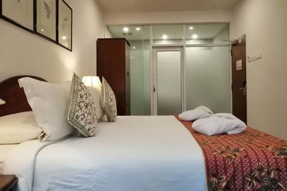 Une chambre d’hôtel avec un lit, des oreillers, une table de chevet, une lampe, une armoire et une porte.