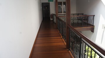 A wooden corridor with a metal railing, a fire extinguisher, and a door labeled "KELUAR".
