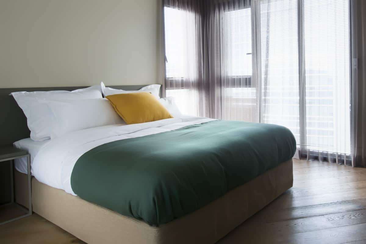 A neatly made bed with white and green bedding, a mustard yellow pillow, and a wooden headboard.