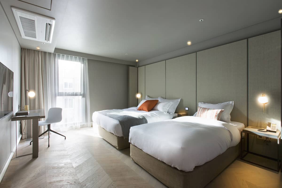 A modern hotel room with two beds, a desk, and a chair.