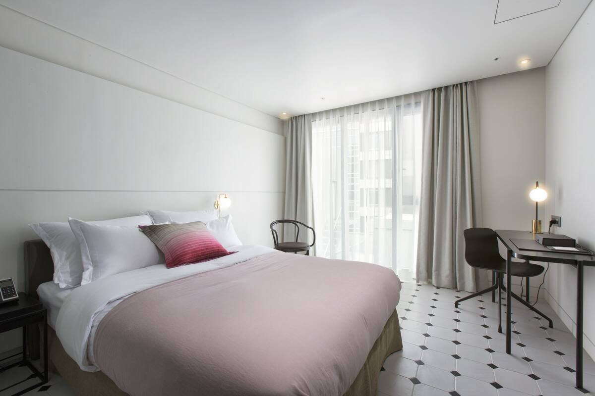 A hotel room with a bed, a desk, a chair, and a window with curtains.