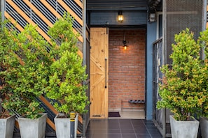 Una puerta de madera que da paso a un interior con paredes de ladrillo, con plantas en macetas a cada lado.