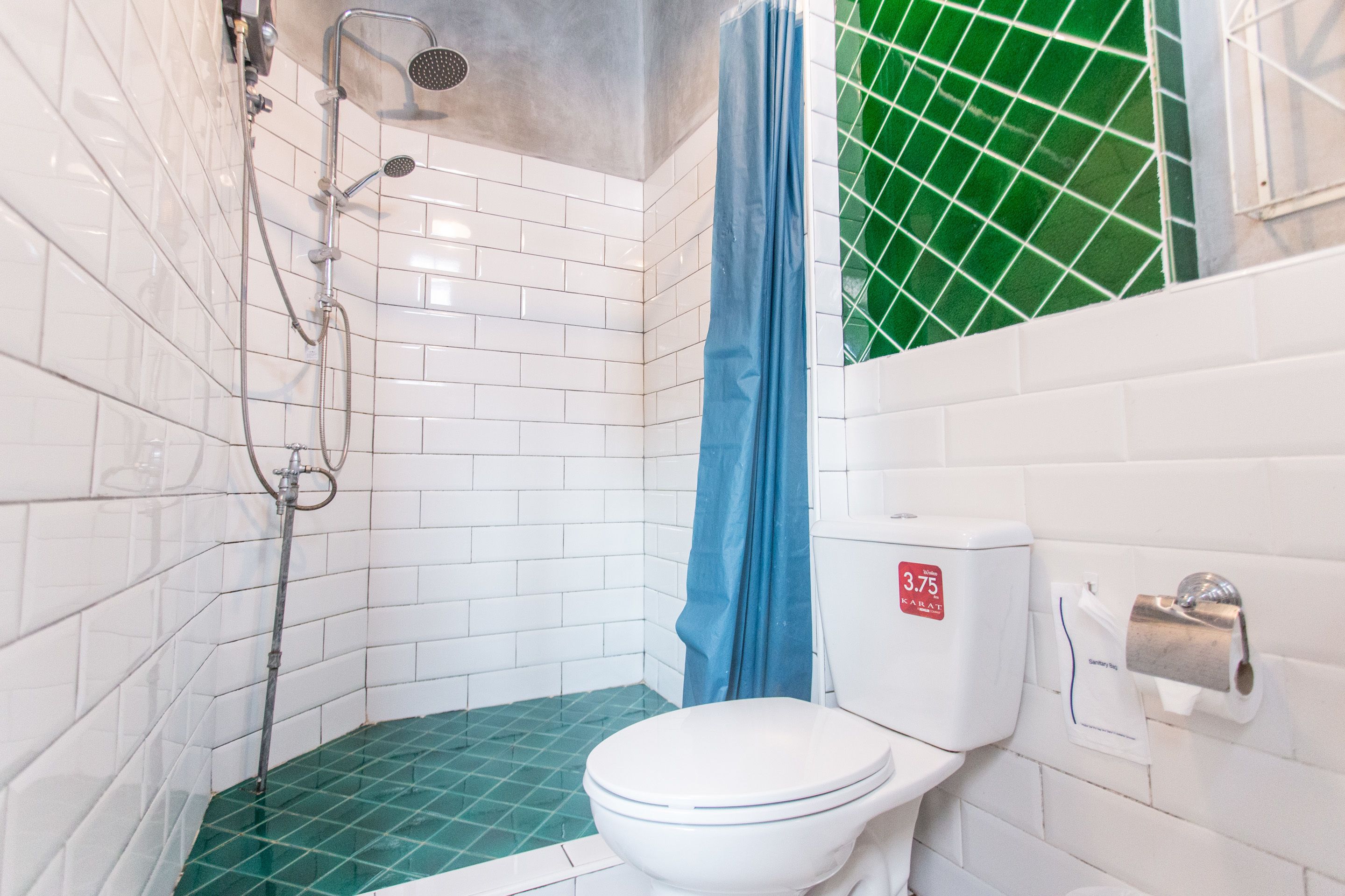A small bathroom with a white toilet, a shower with a blue curtain, and a green-tiled floor.