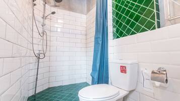 A small bathroom with a white toilet, a shower with a blue curtain, and a green-tiled floor.