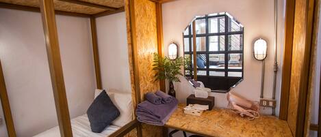 Habitación pequeña con literas, una mesita con una planta y ventana con vistas al exterior.
