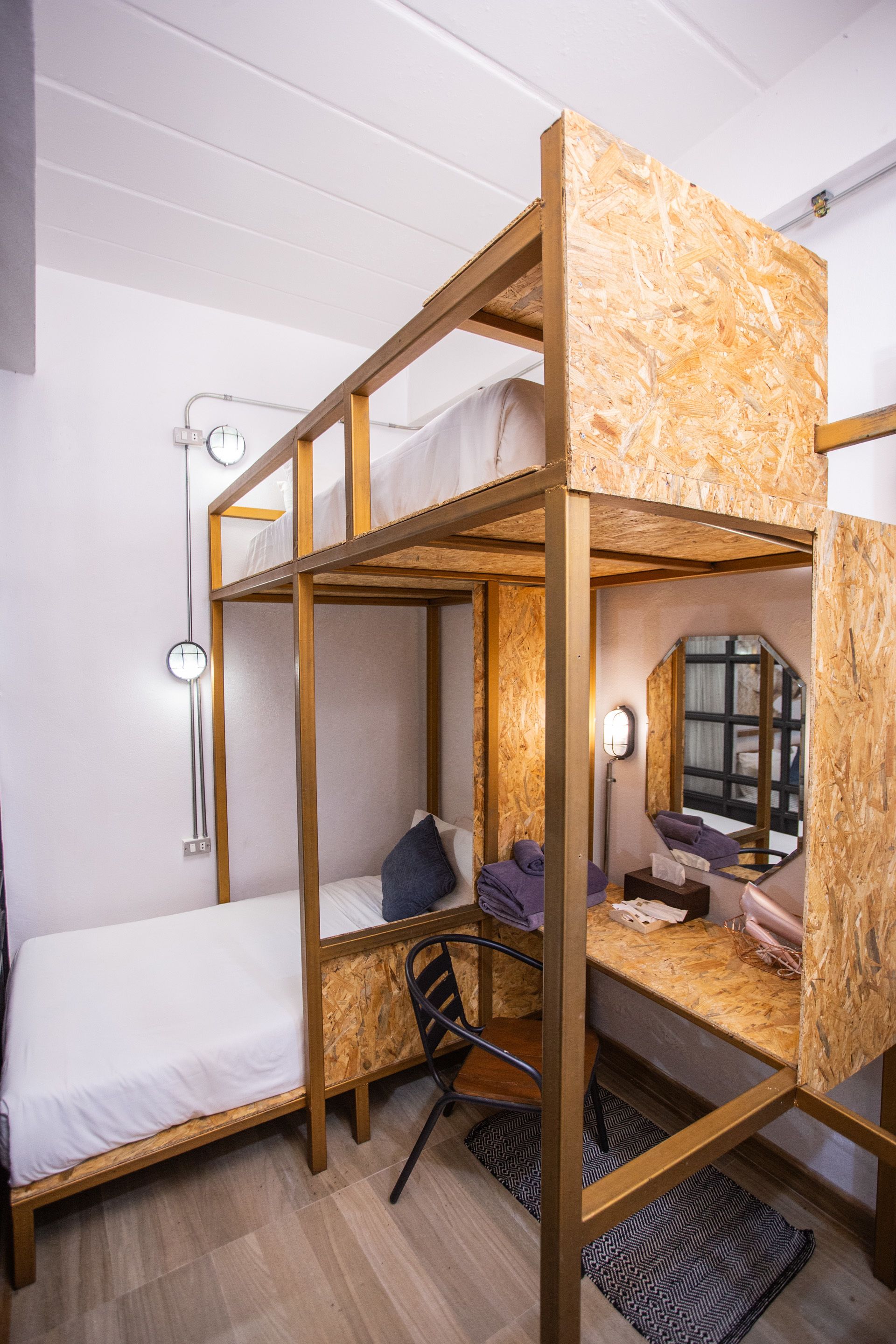 Habitación con literas de madera, un escritorio con silla, una lámpara y un espejo.