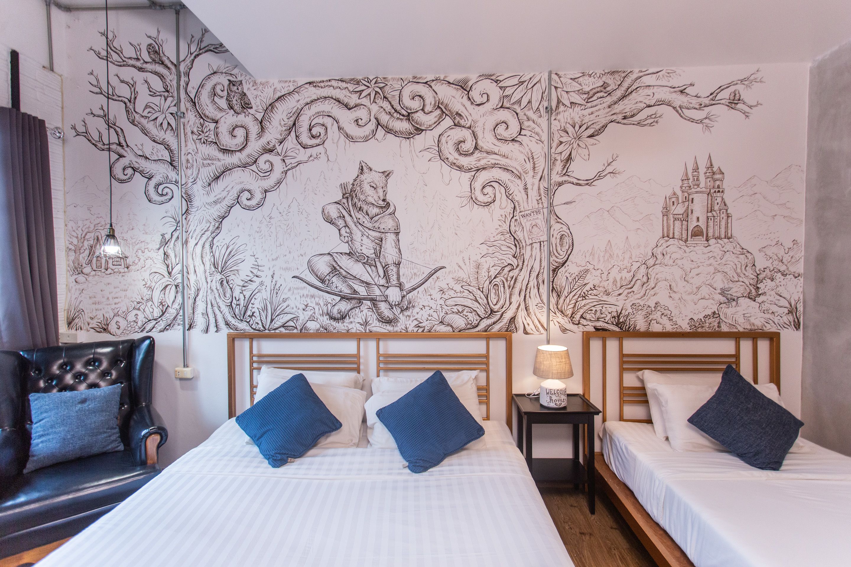A hotel room with two beds, a large wall mural, a leather armchair, and a small table with a lamp.