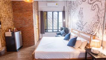 A bedroom with a brick wall, a bed with white bedding, a desk with a lamp, and a window with curtains.