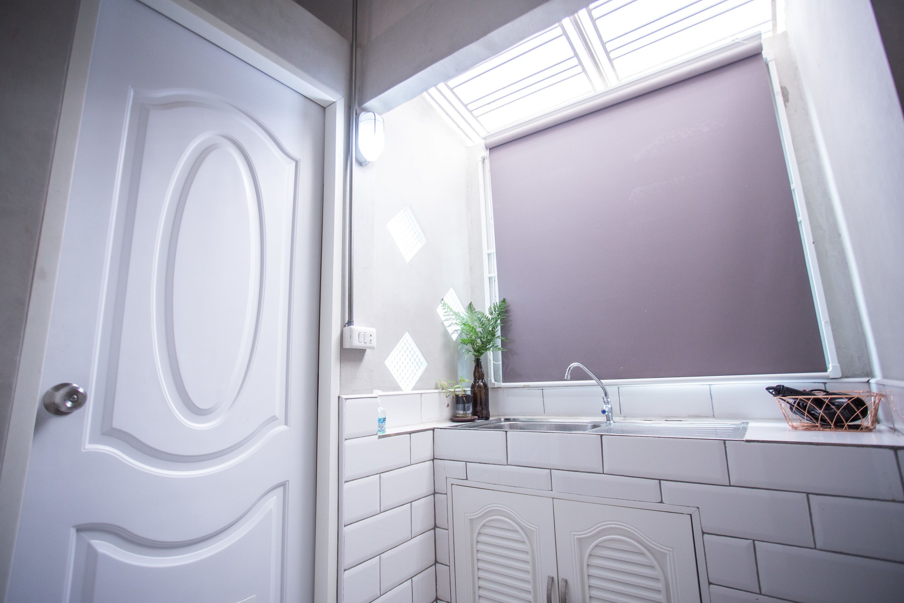 A bathroom with a white door, a window above the sink, and a mirror.