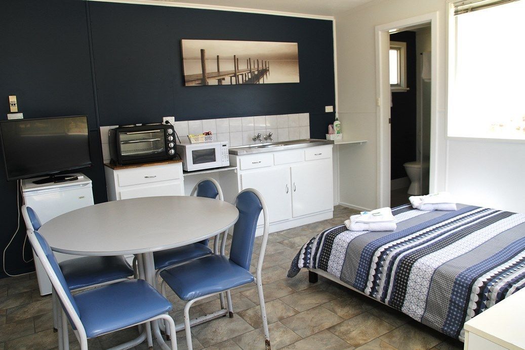 Une pièce compacte comprenant un lit, une petite table avec des chaises, un coin cuisine équipé d’un four à micro-ondes, d’un grille-pain et d’une télévision.
