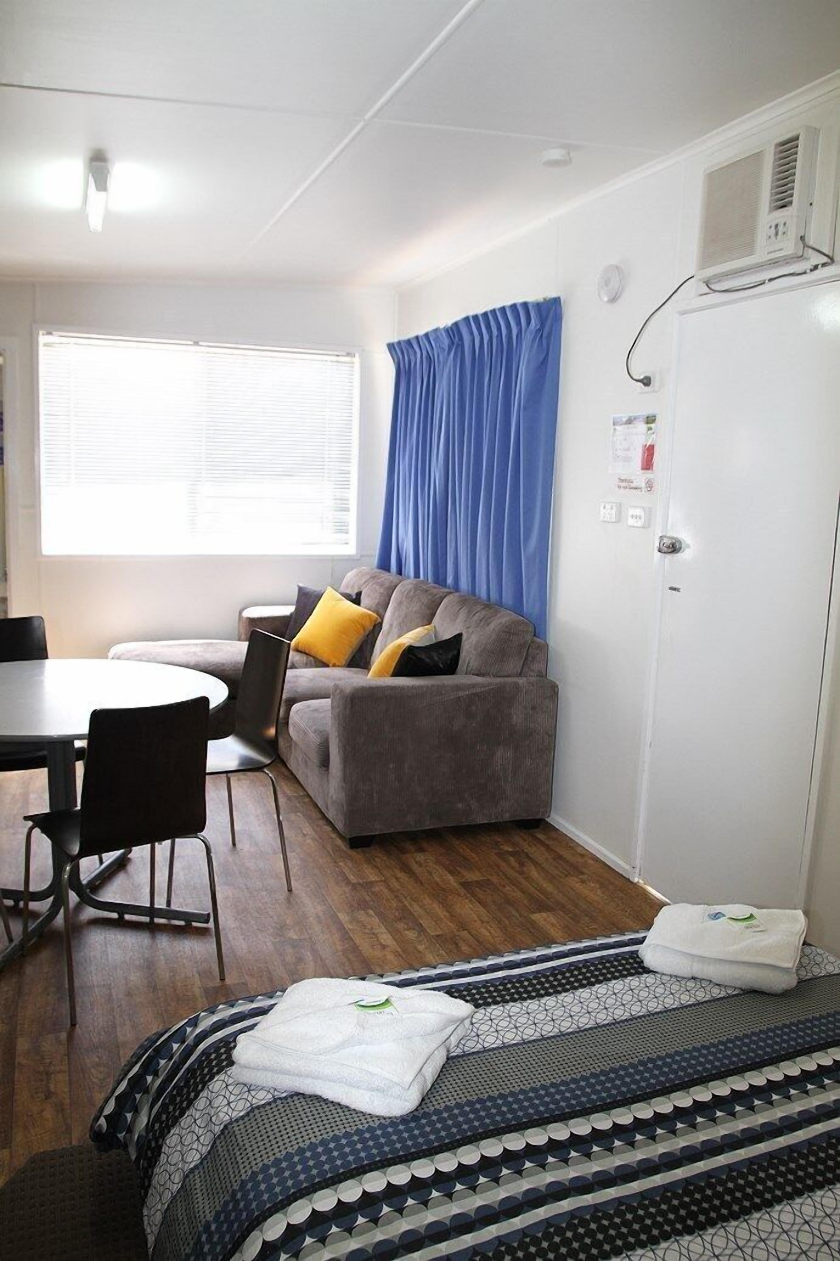 Una habitación con un sofá gris, una mesa de comedor redonda y una cama con ropa de cama estampada.