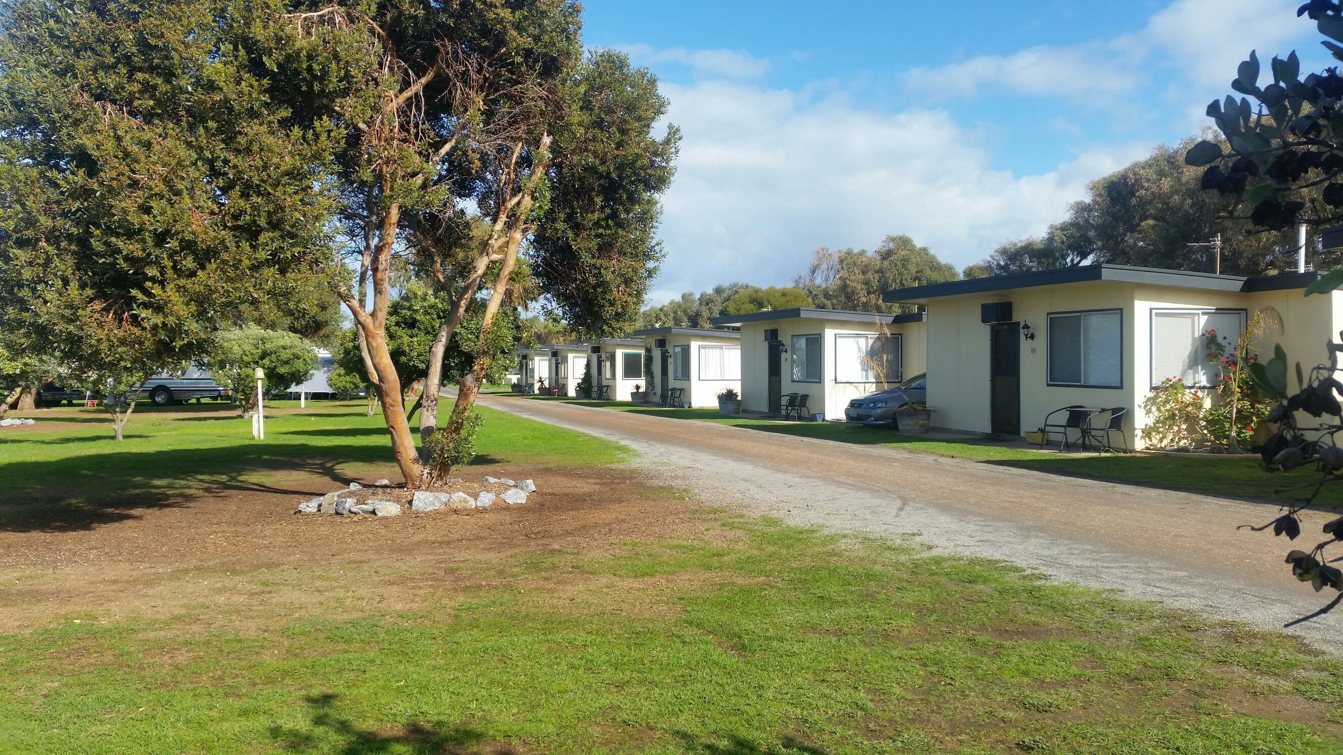 A row of mobile homes with a gravel path leading to them, surrounded by grass and trees.