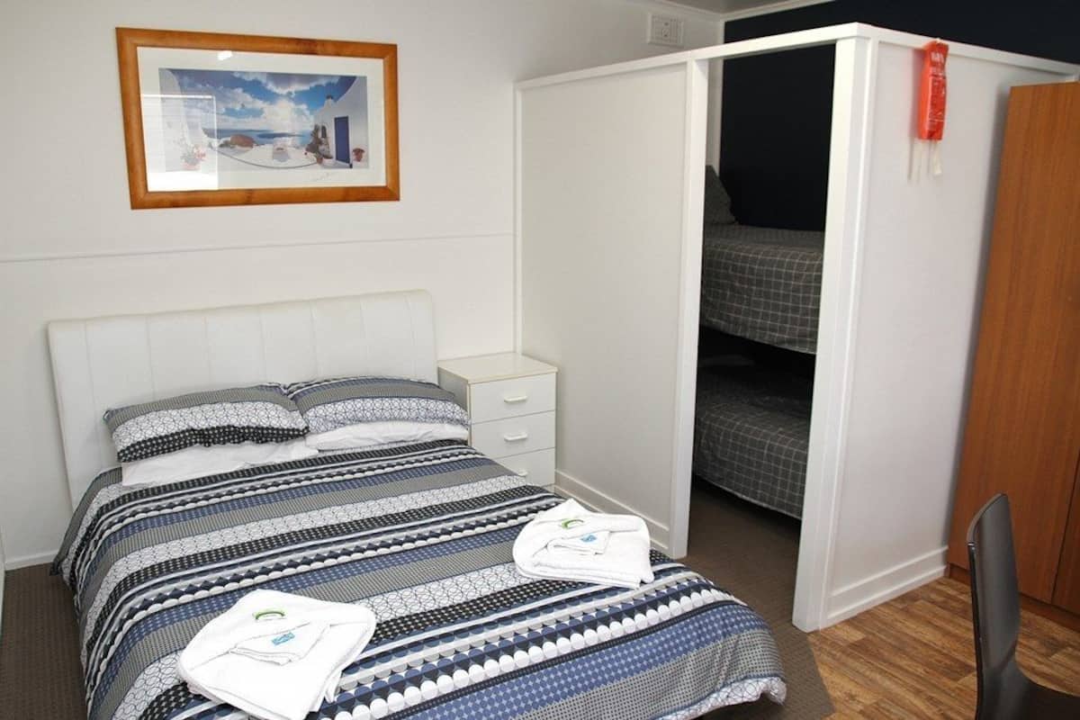 A bedroom with a bed, a white wardrobe, a nightstand, and a framed picture on the wall.