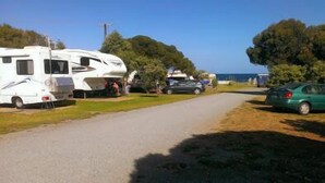 Un camping con vehículos recreativos y automóviles estacionados a lo largo de una carretera, rodeado de árboles y un cielo despejado.